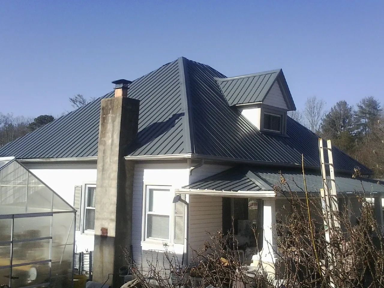 Dark blue standing seam metal roof on a white farmhouse with dormer — Slate & Tile Roof Repair by Roofing Brothers in Carle Place