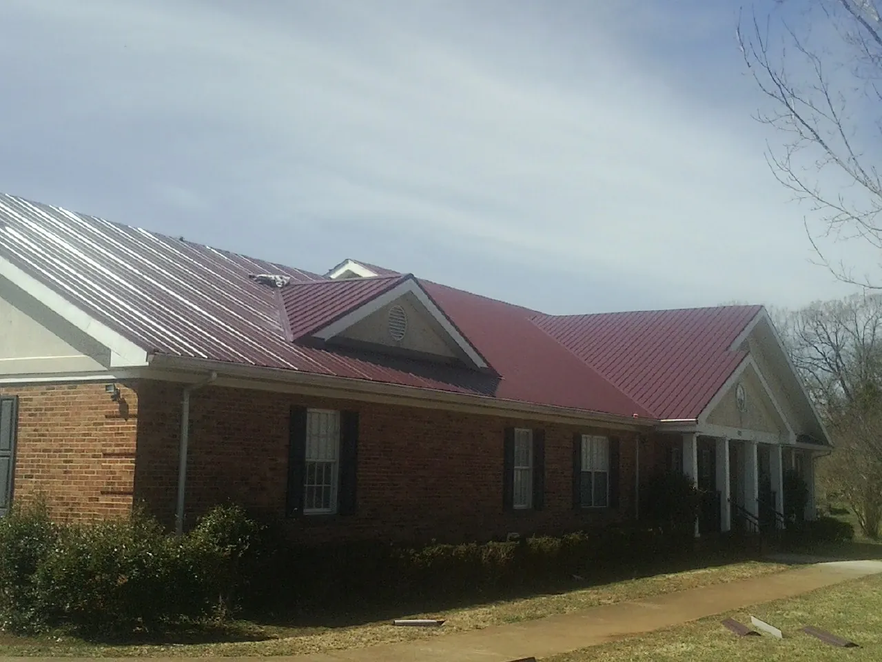 Red metal roof with gabled entries on a long brick building, from a Hail Damage Roof Repair job in Carle Place
