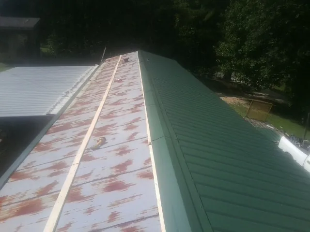 Old rusted panels beside newly installed green metal roofing — Wind Damage Roof Repair by Roofing Brothers in Carle Place