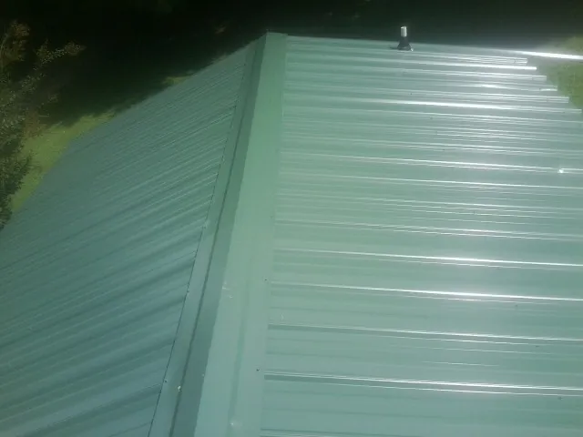 New green metal panels meeting at the ridge of a roof — Flat Roof Repair work by our crew in Carle Place