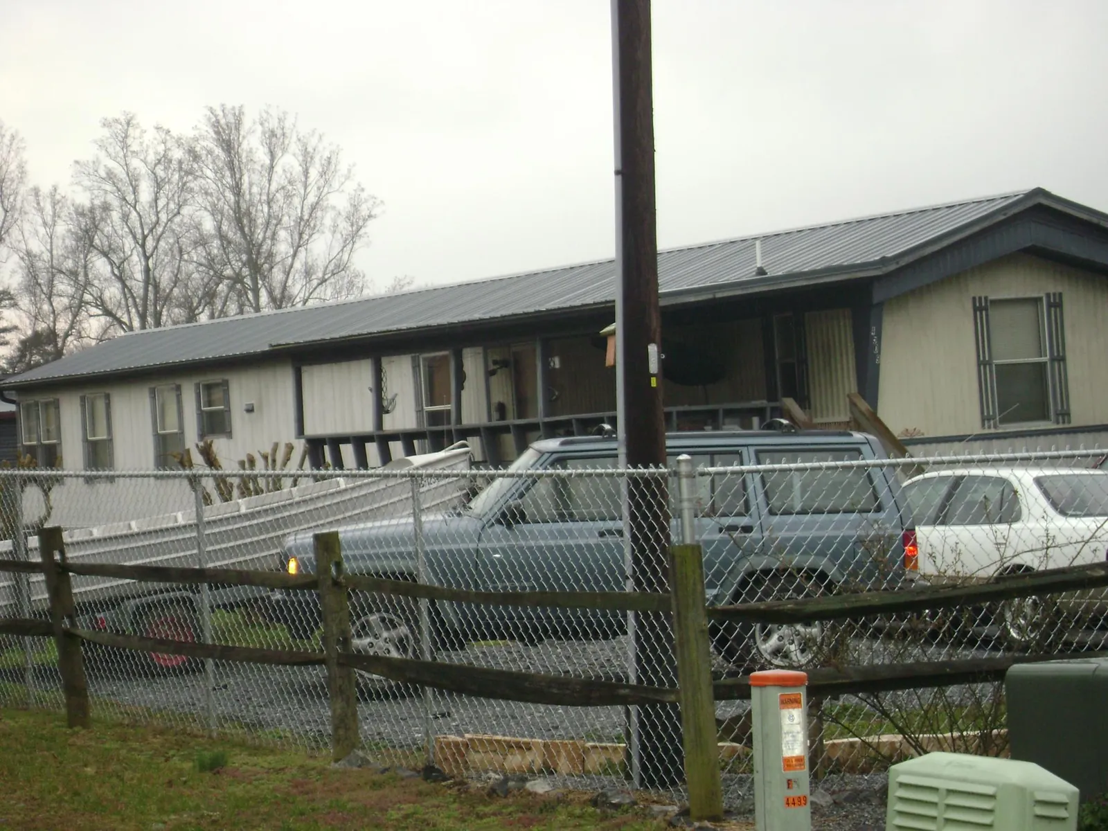 Dark metal roof on a long single story building behind a chain link fence in Carle Place