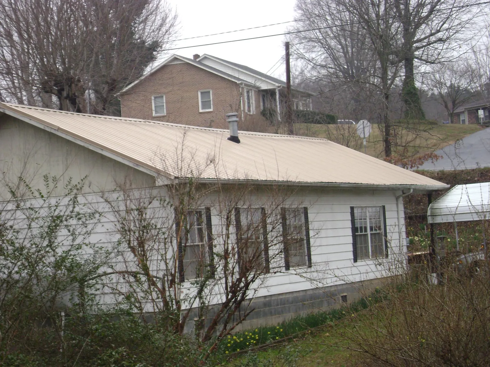 Tan metal roof on a white sided house set into a hillside — Commercial Roofing by Roofing Brothers in Carle Place