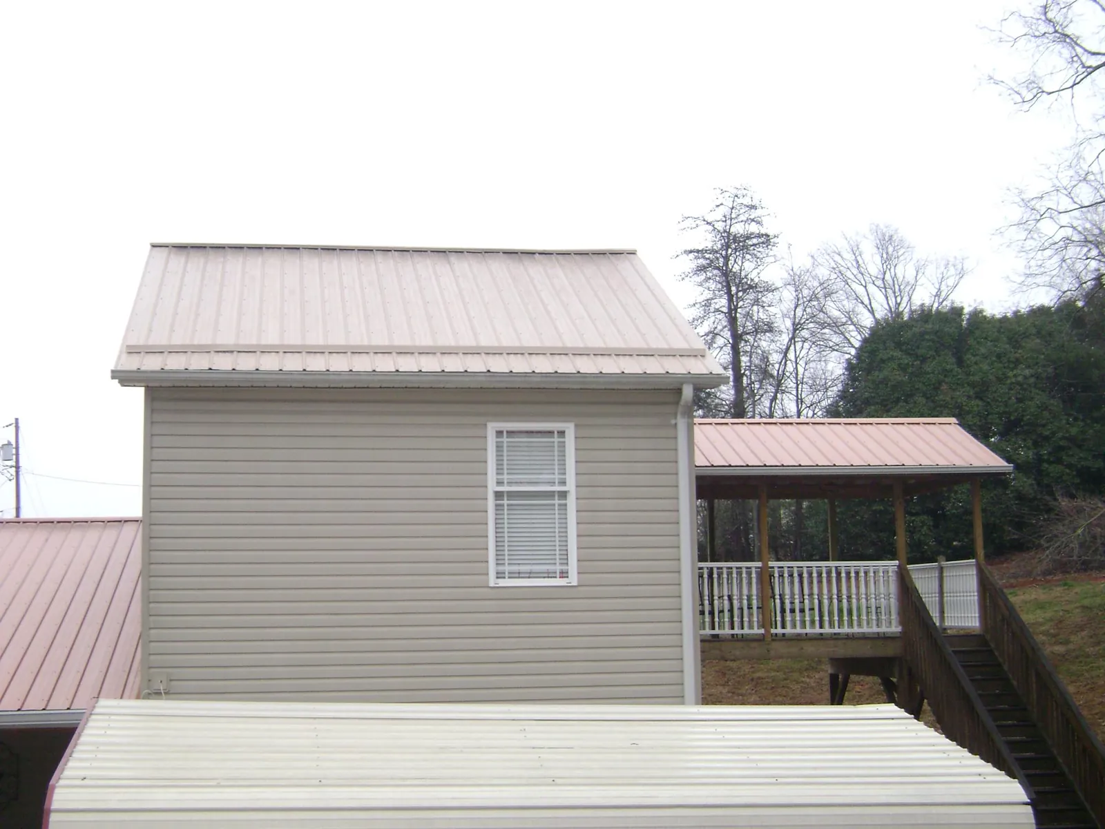 Tan metal roofs on a two story addition and attached porch, from a Roof Replacement job in Carle Place